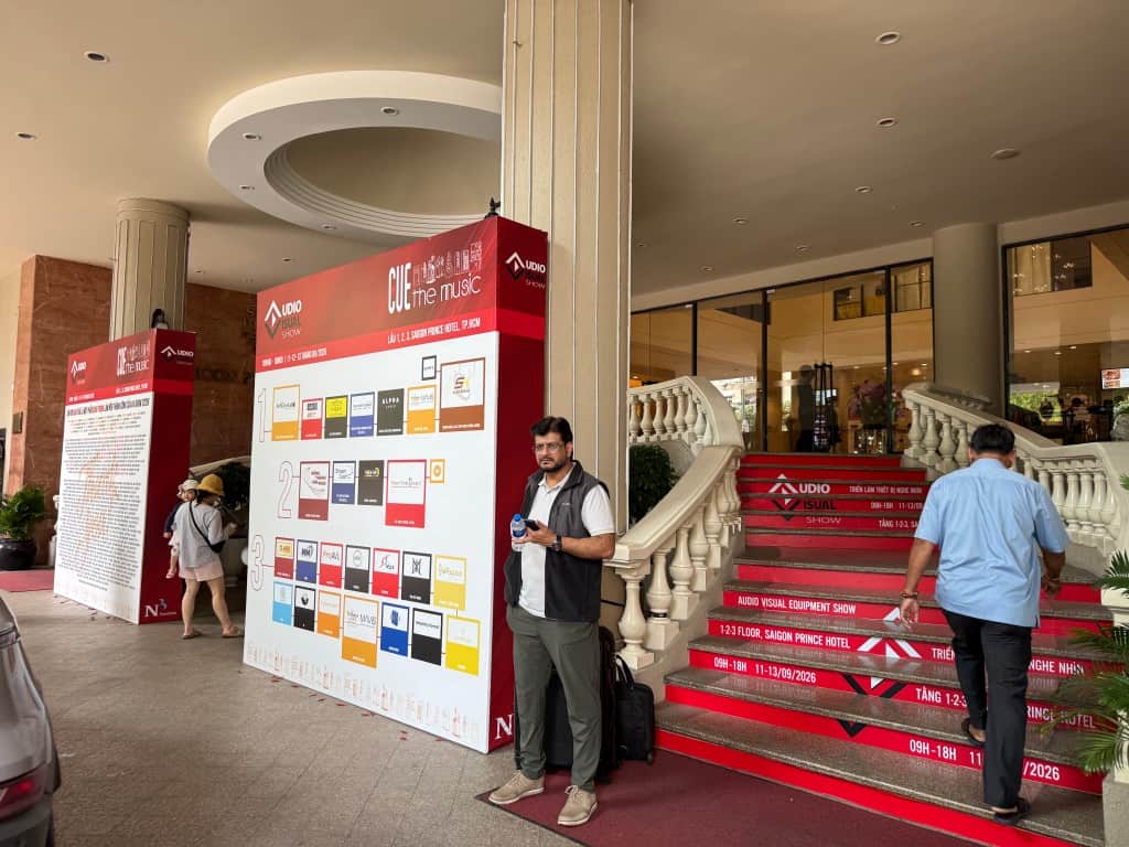 People at conference entrance with audio visual display boards and stairs.